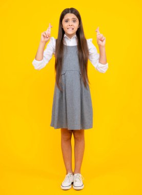 Portrait of adorable little teenager gitl standing with biting lips and crossing fingers, wishing for good luck. Childhood dreams and hopes