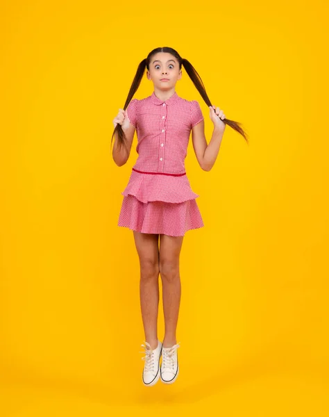 Amazed teenager. Excited teen girl. Full length funny teenager kid jump enjoy rejoice win isolated on yellow background. Small child girl in summer dress jumping