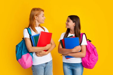 Mother and daughter, happy family preparing for school. Little girl with mother learning, preparing to school on isolated yellow studio background