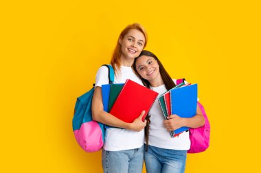 Okul, öğrenme ve eğitim konsepti. Okul çantalı ve kitapları öğrenmeye hazır anne-kız okul kızları. Okula dönelim. Anne ve çocuk izole edilmiş sarı stüdyo geçmişinde