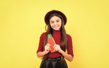 Şapkalı neşeli çocuk sarı arka planda şampuan şişesi, saç bakımı.