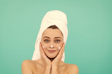 Neşeli genç bir kadın mavi arka plana yüz kremi sürüyor..