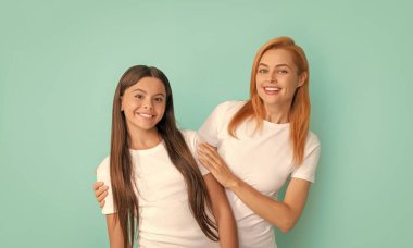 loving cheerful mother embrace daughter in white shirts on blue background, happiness.