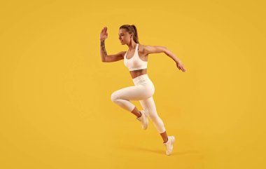Spor kıyafetleri içinde koşan fitness kızı koşucusu sarı arka planda.