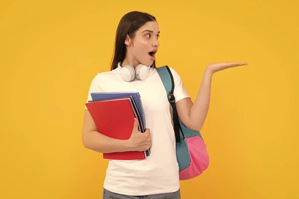 private teacher with copybooks and headphones. back to school. modern education concept. presenting product on copy space. amazed student hold notebook. girl holding notebook on yellow background.