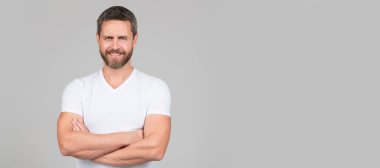 Happy confident man smile keeping arms crossed in white tshirt grey background, guy. Man face portrait, banner with copy space