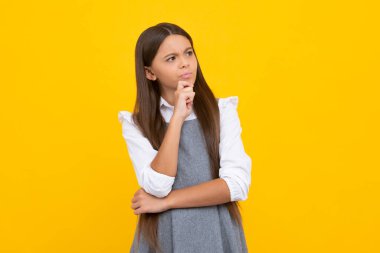 Teenager girl 12, 13, 14 years old thinking against yellow background. Child think and creative idea concept. Thinking face, thoughtful emotions of teenager girl
