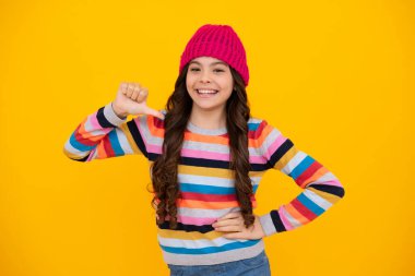 Beautiful winter kids portrait. Teenager girl posing with winter sweater and knit hat on yellow background. Happy teenager, positive and smiling emotions of teen girl