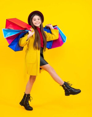 Happy teenager portrait. Child girl hold shopping bag enjoying sale isolated on yellow background. Run and jump. Portrait of teenager girl is ready to go shopping. Smiling girl