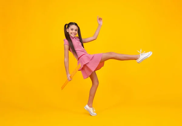 Measuring school equipment. Schoolgirl holding measure for geometry lesson, isolated on yellow background. Student study math. Crazy jump, jumping kids