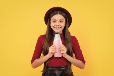 Şapkalı mutlu kız şampuanı tutuyor. Gençler için kozmetik ürünler sunuyorum. Çocuk duş jeli kullanıyor. Kuaförde uzun saç şampuanı. Saç kremi kullanan bir çocuk. Günlük alışkanlıklar ve kişisel bakım.