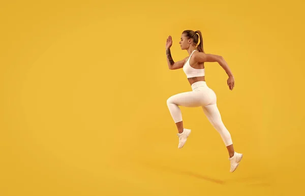 sport girl runner running on yellow background with copy space.