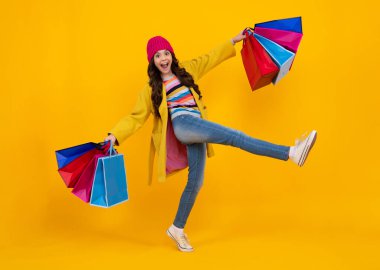 Autumn shopping sale. Teen girl holding shopping bags, isolated on studio background. Run and jump. Happy teenager, positive and smiling emotions of teen girl