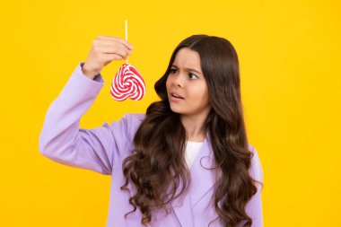 Teen girl hold lollipop caramel on yellow background, candy shop. Teenager with sweets suckers