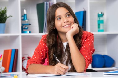 School student writing in exercise book, studying in classroom. Happy schoolgirl