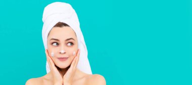 cheerful young lady apply face cream on blue background. Beautiful woman isolated face portrait, banner with mock up copy space