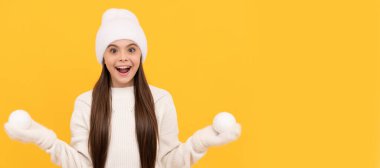 Winter girl. amazed child in winter hat and gloves hold snowballs on yellow background. Banner of christmas child girl, studio kid winter portrait with copy space