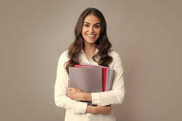 Portrait of student woman. College or high school ducation. Young woman with notebooks smiling at camera on gray studio background. Young female university student