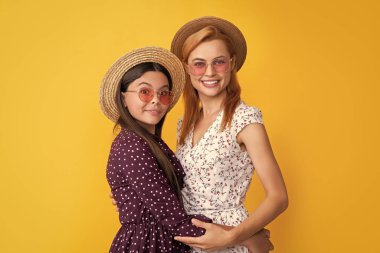 Sarı arka planda hasır şapkalı gülümseyen anne ve çocuk..