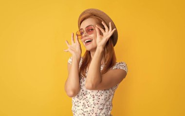 Hasır şapkalı ve sarı arka planda güneş gözlüklü genç bir kadın..