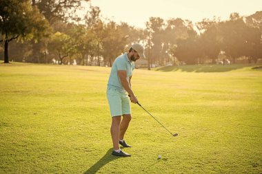 Profesyonel golf sahasında erkek golfçü. Golf sopasıyla şapkalı golfçünün portresi. İnsanların yaşam tarzı. Sakallı bir adam yeşil çimlerde oyun oynuyor. Yaz etkinliği. Profesyonel spor..