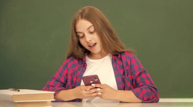 Mutlu çocuk akıllı telefondan konuşuyor. Sınıfta, tahtada. Mesaj var..