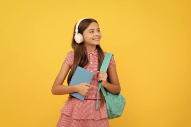 Kulaklıklı mutlu okul çocuğu sırt çantası, çalışma kitabı, kitap taşıyor..