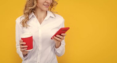happy blonde woman with coffee cup chatting on phone on yellow background.