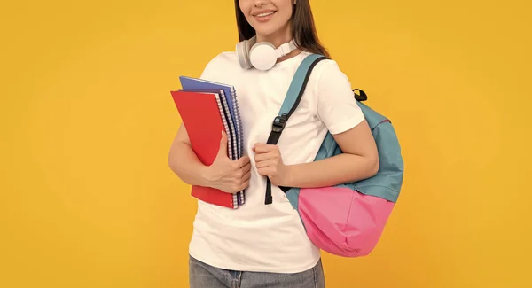 リュックとヘッドフォンを持つ正の若い女の子は黄色の背景にワークブックを保持します — ストック写真