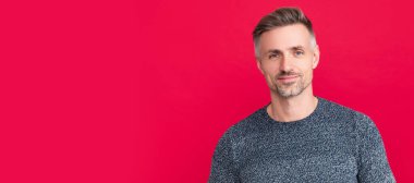 Man face portrait, banner with copy space. positive grizzled guy in sweater on red background,
