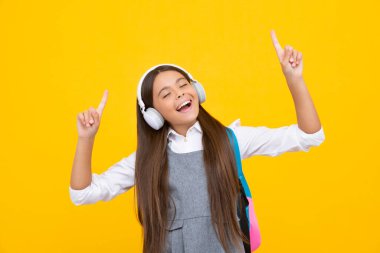 Amazed child singing. School girl, teenager student in headphones on yellow isolated studio background. Music school concept