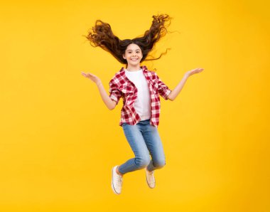 Teenager face with crazy movement hair. Happiness, freedom, motion and child. Young teenager girl jumping in air over yellow background