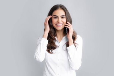 Happy woman talking on phone. Smiling young brunette businesswoman in shirt hold smartphone, isolated on gray background, studio portait. Beauty girl using mobile phone