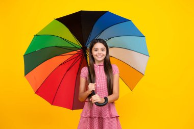 Happy teen girl holding rainbow umbella standing isolated on yellow background, isolated on white. Cheerful teenager child hold parasol. Summer dress