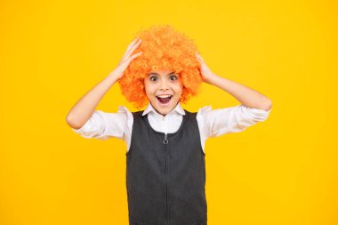 Funny kid in curly redhead wig. Time to have fun. Teen girl with orange hair, being a clown. Excited face, cheerful emotions of teenager girl