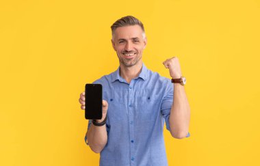 product proposal. advertisement presentation. copy space. happy man presenting phone screen. successful guy showing smartphone on yellow background.