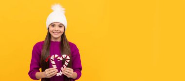 happy new year. happy child in winter hat. kid with candy sticks. teen girl on yellow background. Horizontal poster of isolated child face, banner header, copy space