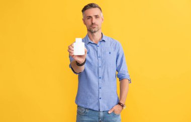 man hold pill jar on yellow background, health.
