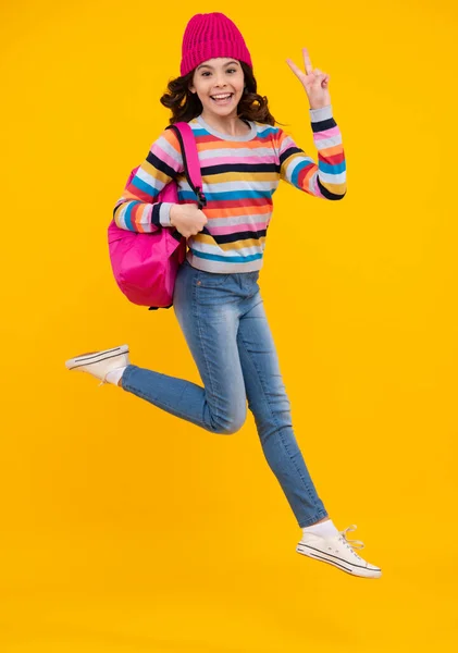 Amazed teenager. Schoolgirl child student with backpack and warn hat, isolated yellow background. Learning and knowledge education concept. Crazy jump and run, jumping kids. Excited teen girl