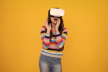 Çocuklar için sanal aletler, boş zaman ve eğitim. Genç kız sarı arka planda izole edilmiş VR gözlükleri kullanıyor. Şaşırmış yüz, şaşırmış genç kız duyguları.