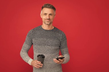Mutlu adam fincandan kahve içiyor ve kırmızı arka planda telefon kullanıyor. İletişim..