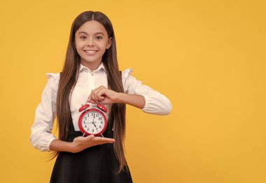 Alarmlı üniformalı neşeli çocuk sarı arka planda saat gösteriyor, dakiklik.