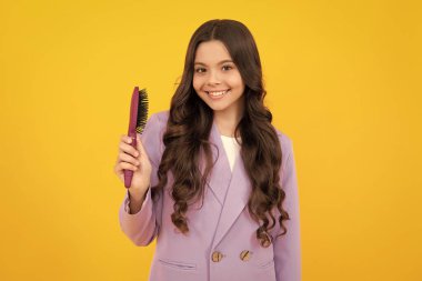 Sarı izole edilmiş stüdyo arka planında saçlarını tarayan genç kız. Saç fırçası olan genç kızlar için kuaför. Çocukların saç stili. Mutlu yüz, pozitif ve gülümseyen genç kız duyguları
