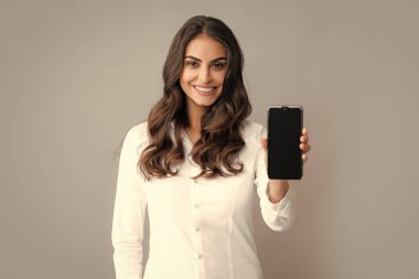 Mutlu genç kadın boş akıllı telefon ekranı gösteriyor. Akıllı telefon, sohbet, SMS konsepti olan mutlu pozitif gülüşlü kadın. Gri arka planda izole edilmiş. Mobil teklif. Cep telefonuyla konuşan kız.