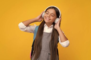 Öğrenmeye hazır kulaklıklı okul kızı. Okul çantalı çocuklar izole sarı stüdyo geçmişine sahipler.