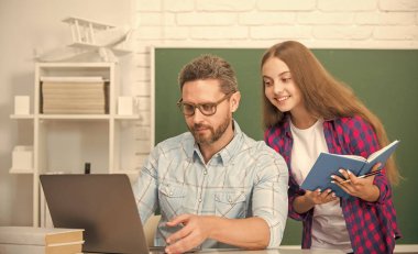 Okulda kitap ve dizüstü bilgisayarla karatahta geçmişi ve ebeveynliği ile meşgul baba ve çocuk eğitimi.