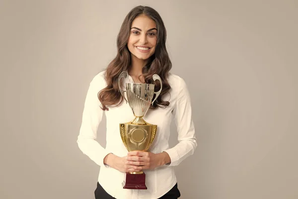 Business woman holding a trophy. Businesswoman concept winner success. Smiling female with trophy isolated on gray background. Successful employee holds winner cup. Award ceremony for winner.