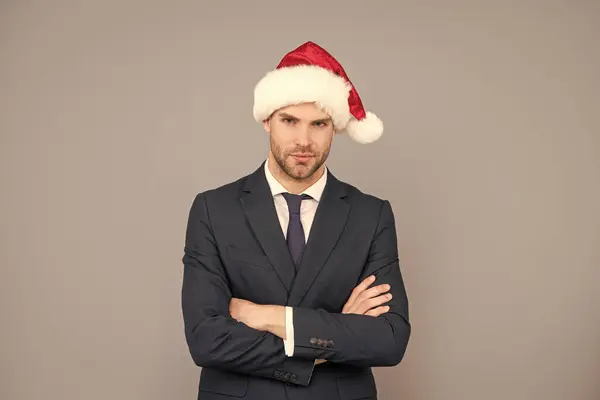 快乐的圣诞节 穿着西服的商人 戴着圣塔克洛斯帽 圣诞节公司派对 一个有着灰色背景的自信的商人 新年快乐 — 图库照片