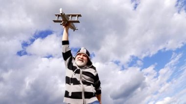 Happy senior man pretend flying on wooden airplane in sky, plane play.