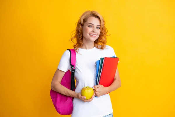 Cute student woman with backpack holds some documents and books over yellow background. Portrait of smiling young woman student in shirt backpack hold notebooks. Education in high school university